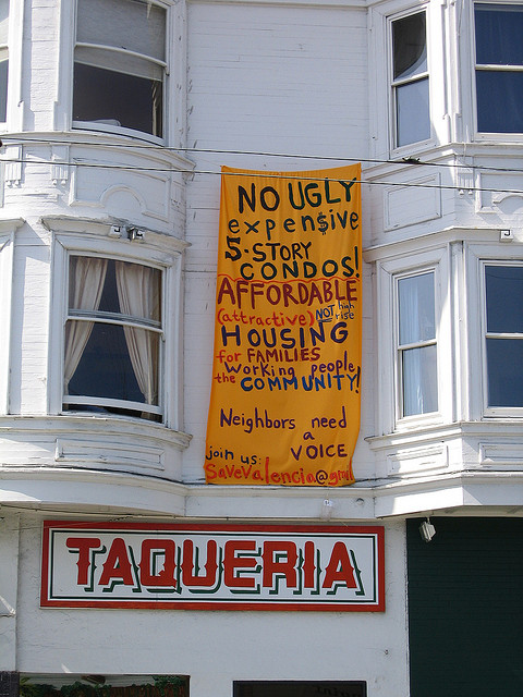 Image of a white building with apartments over a store call Taqueria with a yellow sign that reads 