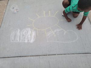 image of child drawing images with chalk on sidewalk by Traviana Archer