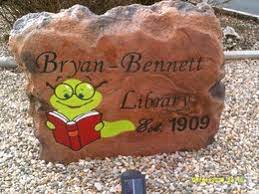 Stone painted brown with an image of a worm with glasses reading a book and the words Bryan Bennett Library est. 1909 painted in black