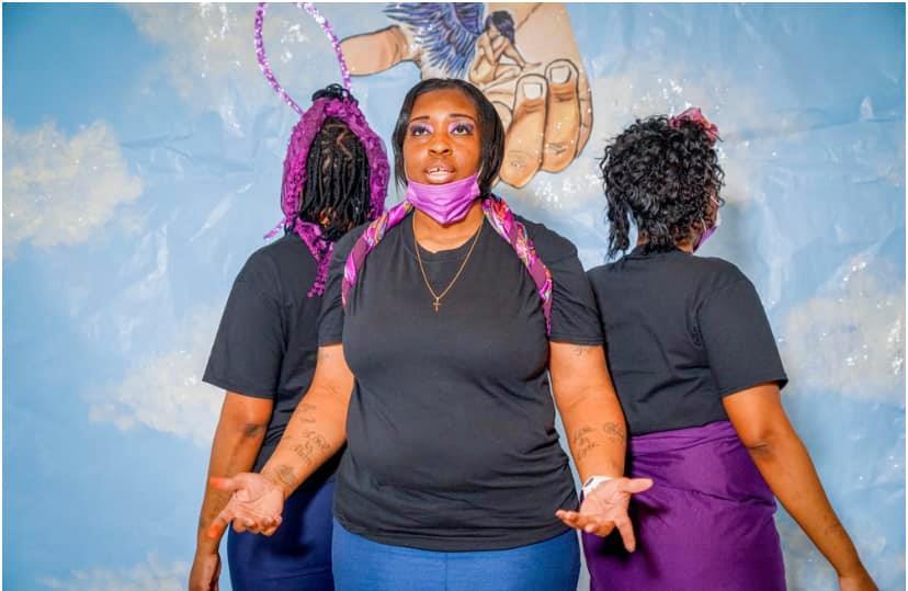 Three women dressed in black and purple perform a poem for the camera