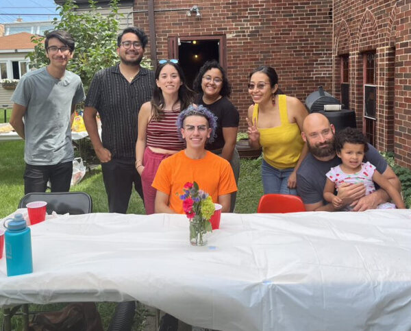 A group of people gathered behind a picnic table with a white table cloth on it