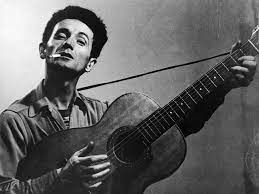 Woody Guthrie pictured holding a guitar while smoking a cigarette
