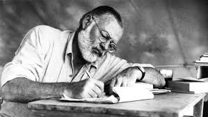 Hemingway writing on a notepad while sitting at a desk